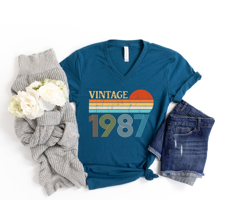 Peut inclure: T-shirt bleu sarcelle &agrave; col en V avec un graphique de coucher de soleil vintage et le texte "Vintage 1987".