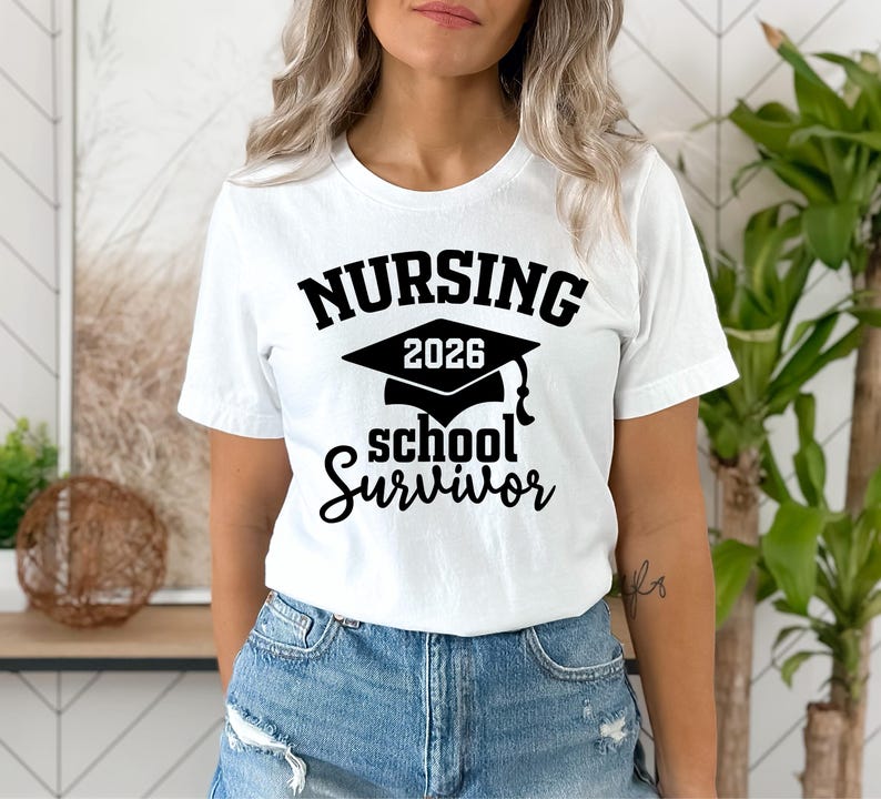 May include: White t-shirt with the text "NURSING 2026 school Survivor" in black. The design includes a graduation cap. The model is wearing blue denim jeans.