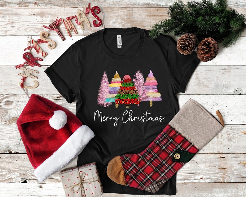 Puede incluir: Camiseta negra con un gr&aacute;fico de tres &aacute;rboles de Navidad coloridos y el texto "Feliz Navidad".