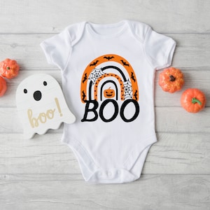 May include: White baby onesie with an orange and black rainbow design featuring a pumpkin, spiderwebs, and bats. The text "BOO!" is written in black below the rainbow.