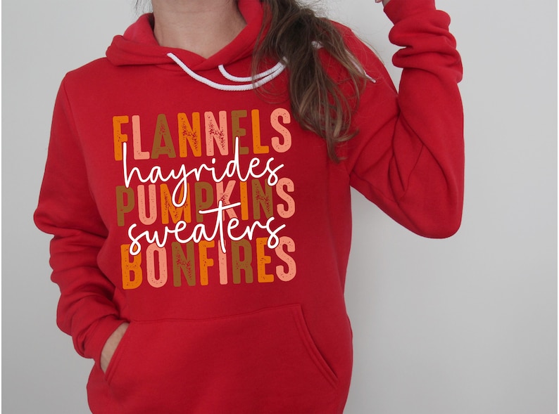 May include: A red hoodie with a white drawstring and a front pocket. The sweatshirt displays the words "FLANNELS, hayrides, PUMPKINS, sweaters, BONFIRES" in autumnal colours.