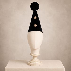 A white mannequin head wearing a black party hat with two gold buttons on the front.