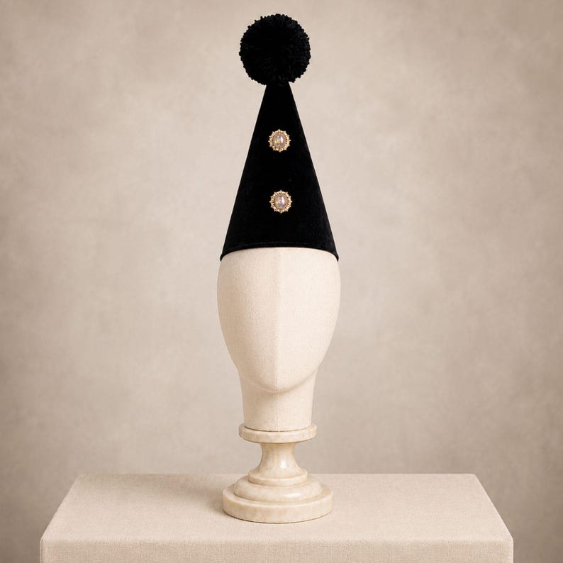 A white mannequin head wearing a black party hat with two gold buttons on the front.