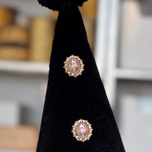 two gold-colored earrings with a floral design, displayed on a black velvet stand.