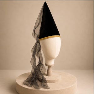A mannequin head wearing a black pointed hat with a long, flowing veil draped over it, displayed on a round platform.