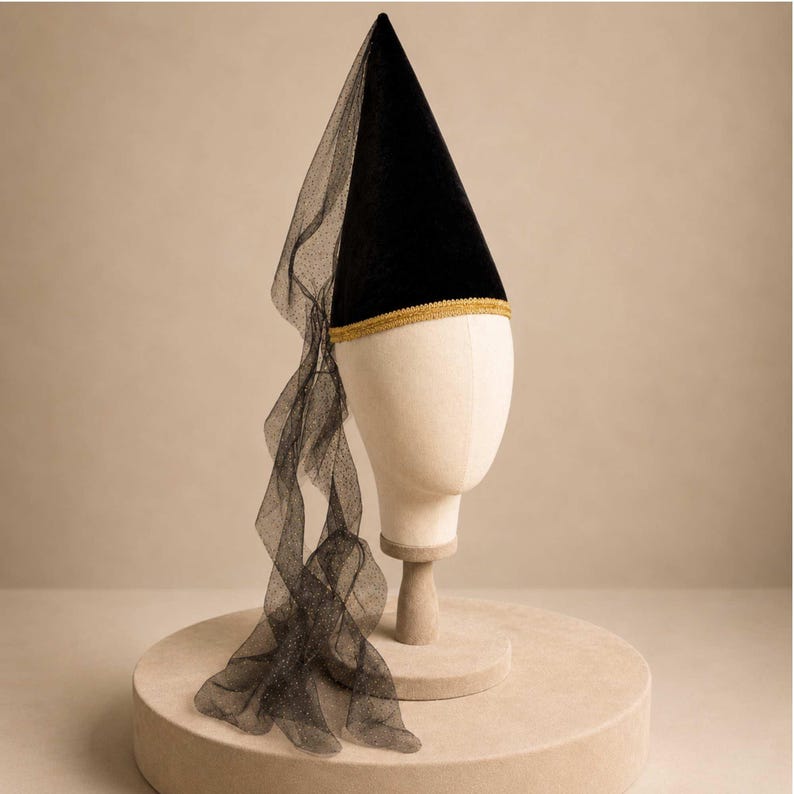 A mannequin head wearing a black pointed hat with a long, flowing veil draped over it, displayed on a round platform.