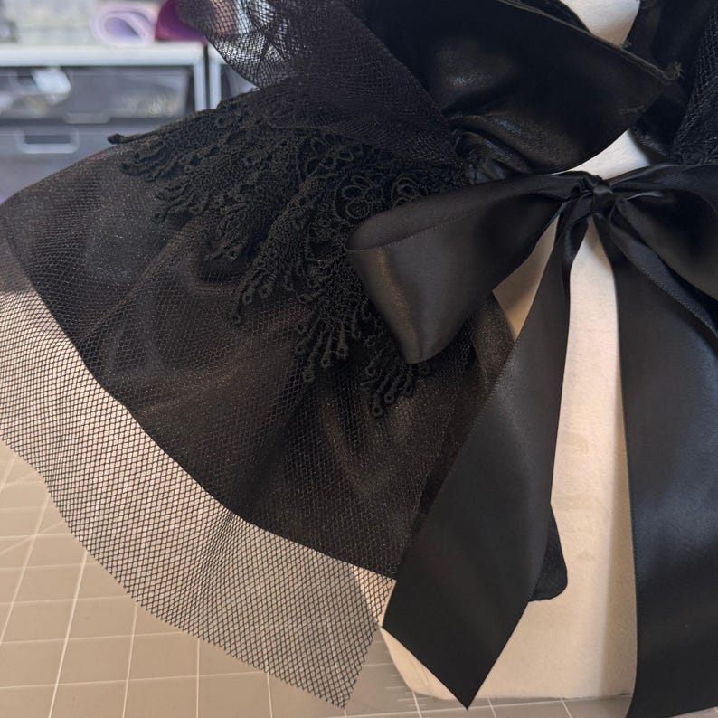 a close-up view of a black lace and black satin bow on a white fabric.