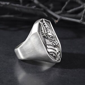 May include: A silver ring with a detailed design of a wolf's head on a shield.