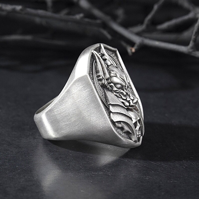 May include: A silver ring with a detailed design of a wolf's head on a shield.