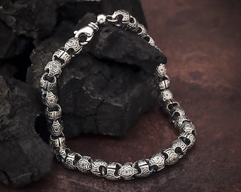 May include: A silver chain bracelet with a detailed, ornate design. The bracelet is made of linked, round, silver pieces with a floral pattern.