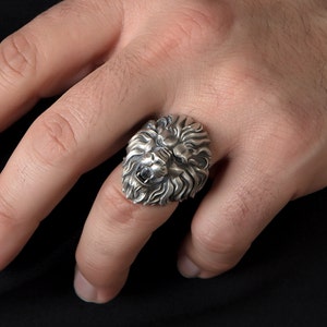 Puede incluir: Un anillo de plata con un dise&ntilde;o detallado de cabeza de le&oacute;n. La boca del le&oacute;n est&aacute; abierta y sus dientes son visibles.