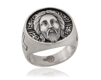 May include: A silver ring with a detailed image of Jesus' face on the front. The ring has a cross design on the side.