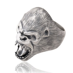 Könnte beinhalten: Ein silberner Ring mit einem detaillierten Gorillakopf-Design. Der Mund des Gorillas ist geöffnet und zeigt seine Zähne. Der Ring ist aus Metall gefertigt und hat eine strukturierte Oberfläche.