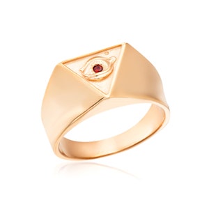 Puede incluir: Un anillo de oro con una parte superior triangular que presenta un dise&ntilde;o de ojo que todo lo ve con una piedra preciosa roja en el centro.
