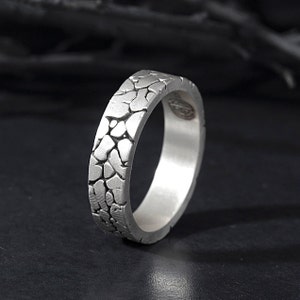 May include: A silver ring with a textured, cracked surface design. The ring is a simple band with a smooth interior.
