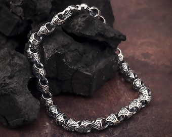 May include: A silver chain bracelet with a detailed, ornate design. The bracelet is made of linked, round metal pieces with intricate patterns.