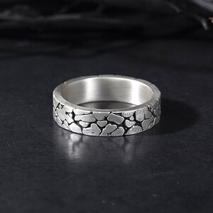 May include: A silver ring with a textured, cracked surface design.