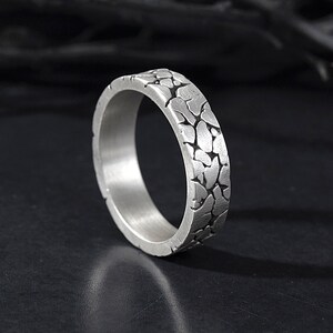 May include: A silver ring with a textured, cracked surface design.