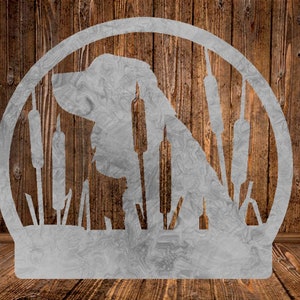 May include: A metal silhouette of a dog with its head turned to the side, standing in a field of tall grass. The silhouette is in a circular frame.