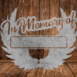 May include: A metal sign with the words "In Memory of" and a blank space for a name. The sign is in the shape of wings and is against a wood background.