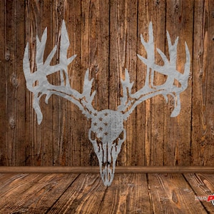 以下が含まれることがあります： アメリカの旗の形にカットされた、角のある金属製の鹿の頭蓋骨。頭蓋骨は銀色で、星は濃い青色の背景に対して白く描かれている。角も銀色です。頭蓋骨は木製の壁に取り付けられています。