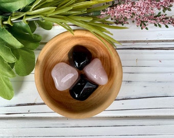 Pode incluir: Uma tigela de madeira cheia de três pedras polidas: duas pretas e uma rosa.
