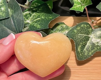 May include: A heart-shaped yellow calcite crystal. The crystal is smooth and polished, with a warm, golden hue.