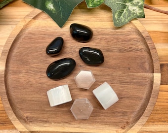 Puede incluir: Una colección de siete piedras pulidas dispuestas sobre una superficie de madera. Cuatro piedras son lisas, redondeadas y de color negro. Tres piedras son blancas, dos cilíndricas y una hexagonal plana, con una apariencia translúcida.