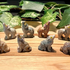 May include: Eight small, hand-carved stone wolf figurines in various shades of brown, gray, and white. The wolves are all howling and have yellow eyes.