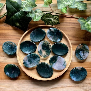 May include: A collection of ten green and white agate palm stones arranged on a wooden surface. The stones are smooth and polished, with a variety of patterns and swirls.