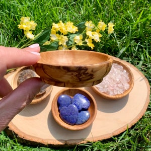 K&ouml;nnte beinhalten: Vier kleine Holzschalen mit verschiedenen Kristallen. Die Schalen sind auf einer Holzscheibe angeordnet. Die Schalen enthalten blaue herzf&ouml;rmige Steine, rosa Kristalle und eine versteinerte Muschel.