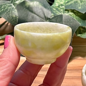 May include: A small, white and green jade bowl with a smooth, rounded surface. The bowl is made of natural stone and has a subtle, mottled pattern.