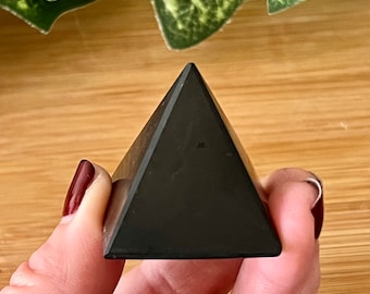May include: Black obsidian pyramid crystal, a dark, polished, triangular shape.