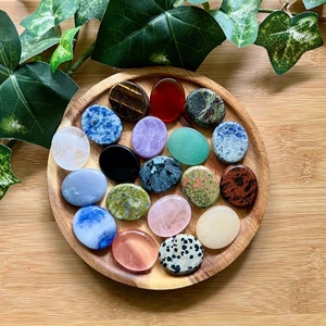 May include: A collection of 18 smooth, oval-shaped polished stones in various colors and patterns, including green, blue, red, purple, black, and white, displayed on a wooden tray.