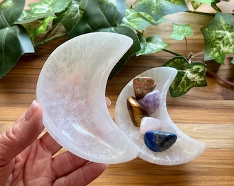 May include: White selenite crescent moon shaped dish with a variety of crystals inside, including amethyst, tiger's eye, rose quartz, and lapis lazuli.
