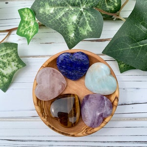 K&ouml;nnte beinhalten: F&uuml;nf herzf&ouml;rmige Kristallsteine in einer Holzschale. Die Steine sind Rosenquarz, Amethyst, Tigerauge, Aquamarin und Lapislazuli.