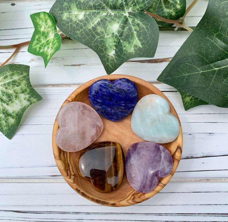 K&ouml;nnte beinhalten: F&uuml;nf herzf&ouml;rmige Kristallsteine in einer Holzschale. Die Steine sind Rosenquarz, Amethyst, Tigerauge, Aquamarin und Lapislazuli.