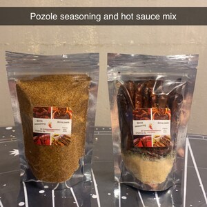 May include: Two clear plastic bags containing a pozole seasoning and hot sauce mix. The seasoning is a light brown powder and the hot sauce mix contains dried red peppers and a light brown powder.