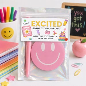 May include: A clear holographic pouch containing a pink pen and a round pink smiley face sticker. The attached label reads: I'M SO EXCITED TO HAVE YOU IN MY CLASS! WELCOME TO 3RD GRADE FROM: MRS. SMITH, featuring colorful illustrations of school supplies.