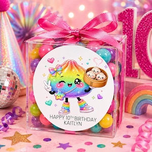May include: A clear square plastic box filled with colorful gumballs, topped with a bright pink satin ribbon. A circular label on the front features a rainbow-colored cartoon dumpling character, a bamboo steamer, and the text HAPPY 10TH BIRTHDAY KAITLYN.