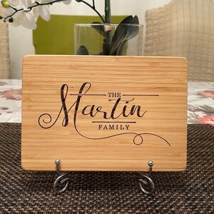 Op de afbeelding: Een gepersonaliseerd bamboe snijplank met de tekst "The Martin Family" gegraveerd in een cursief schrift.