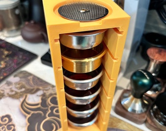 May include: A yellow plastic holder with a stack of five metal coffee filters. The holder has a round, perforated metal disc on top.