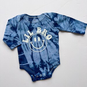 May include: A blue tie-dye long-sleeve baby onesie with the text "Lil Bro" and a white smiley face.