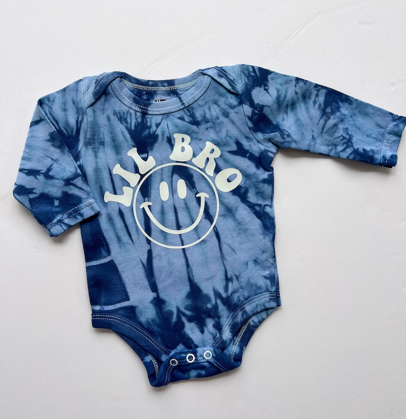 May include: A blue tie-dye long-sleeve baby onesie with the text "Lil Bro" and a white smiley face.