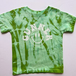 May include: Green tie-dye t-shirt with a white smiley face and the word "GUNNER" in a retro font.