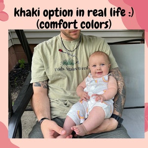 Pu&ograve; includere: Un uomo indossa una maglietta color kaki con la scritta "Dads Against Weed" e tiene in braccio un bambino che indossa un body bianco e grigio con disegni arcobaleno. Il bambino sorride.