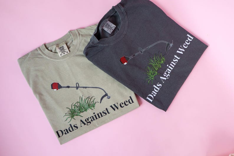 Pu&ograve; includere: Due t-shirt con una grafica di un decespugliatore e il testo "Dads Against Weed". Una maglietta &egrave; verde chiaro e l'altra &egrave; grigio scuro.