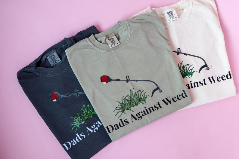 Pu&ograve; includere: Tre magliette con un'immagine di un decespugliatore e il testo "Dads Against Weed". Le magliette sono di colore nero, verde e bianco.