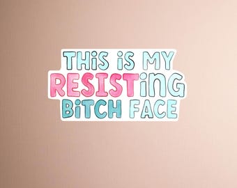 May include: A sticker with the phrase "THIS IS MY RESISTING BITCH FACE" in a playful, handwritten font. The words are outlined in light blue with pink and blue fill, set against a neutral background.