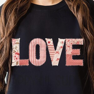 Op de afbeelding: Een zwart sweatshirt met ronde hals en het woord LOVE op de borst. Elke letter is ontworpen met een patchwork-stijl patroon in roze, witte en rode tinten, inclusief bloemen-, streep- en stippenmotieven met zichtbare stiksels.